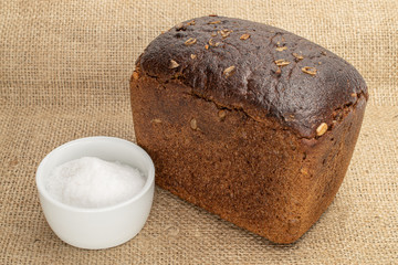 One whole fresh baked dark bread with pinch of salt on jute cloth