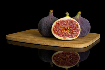 Group of two whole one half of fresh purple fig on bamboo cutting board isolated on black glass