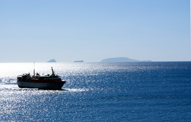 Greece, daybreak. The early morning ferry sails into harbor. A silver, peaceful sea as the ship navigates to the dock. Picture might illustrate travel or, specifically, Greek island hopping.