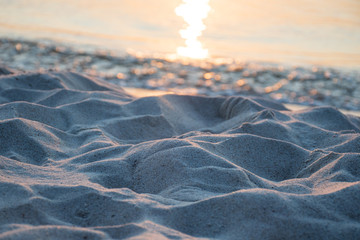 Waves of the sea meet the sand on the shore of a sandy beach on sunset, with reflection of the sun on the water, close up