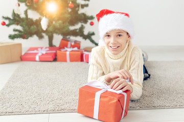 Holidays, christmas, childhood and people concept - smiling happy teen boy in santa hat with gift box over christmas tree background