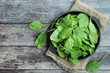 Fresh organic baby spinach leaves on a plate on dark wooden table top view. Healthy and organic food concept.