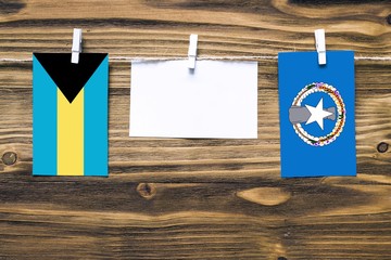 Wall Mural - Hanging flags of Bahamas and Northern Mariana Islands attached to rope with clothes pins with copy space on white note paper on wooden background.Diplomatic relations between countries.