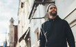 © San4ezz007 - City portrait of handsome hipster man with beard wearing black blank hoodie or hoody and hat with space for your logo or design. Mockup for print