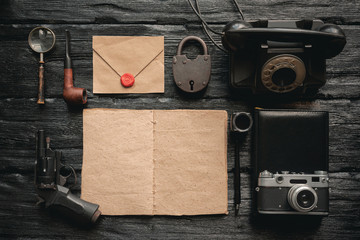 Wall Mural - Open blank page detective book with various equipment around on black wooden table background.