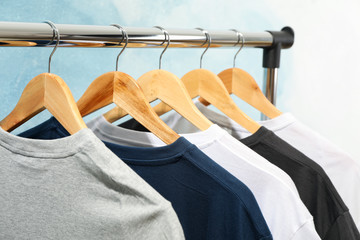 Wall Mural - Rack with blank t-shirts on blue background, close up