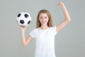 Wall Mural - Football fan. Young woman with a soccer ball raised her hand up in a sign of winning.