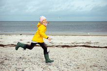 Cheerful Little Girl Running On Water Of Baltic Sea In Rubber Boots At Windy Weather