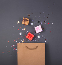 Kraft Paper Bag On Bright Dark Background. With Gift Boxes And Confetti. Black Friday Christmas Gift Preparation Concept.