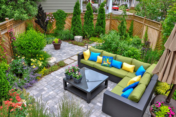 A beautiful small, urban backyard garden featuring a tumbled paver patio, flagstone stepping stones, and a variety of trees, shrubs and perennials add colour and year round interest. 