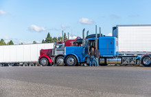 Truck drivers exchange views on the strengths and weaknesses of their big rigs semi trucks standing on truck stop