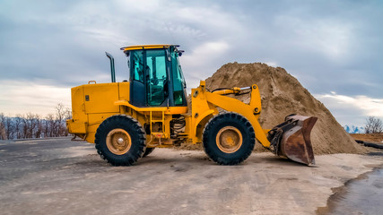 Wall Mural - Panorama Yellow bulldozer on a road with mound of soil and cloudy sky background