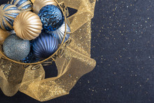 Blue And Gold Christmas Decoration Of Brass Basket Of Ball Ornaments With Soft Focus Dark Blue Background With Gold Glitter And Tulle Ribbon. New Year Greeting. Holiday Concept With Copy Space.