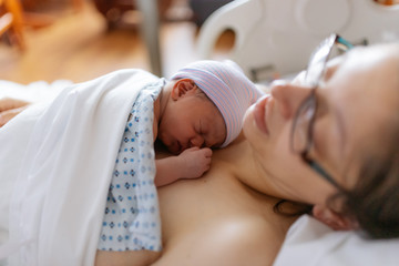 newborn baby in hospital after just being born, mother holding him and breastfeeding in hospital bed