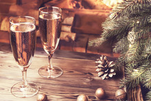 Christmas Composition - Two Glasses With Champagne On A Wooden Table Near A Christmas Tree In A Room With A Burning Fireplace