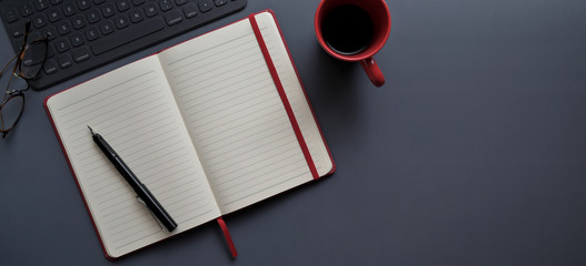 Top view of dark modern workplace with open notebook and red coffee cup