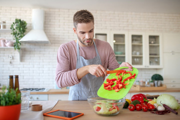 Bearded handsome man cooking veggie salad for dinner