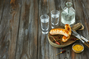 Vodka with fried sausages and sauce on wooden background. Alcohol pure craft drink and traditional snack. Negative space. Celebrating food and delicious.