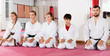 © JackF - Group of children dressed in kimonos sitting on floor at gym with young man trainer