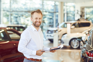 Canvas Print - A car dealer smiling standing in a showroom.