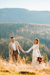 Lovely gorgeous bride and groom walking in sun light holding hands, boho wedding couple