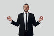© G-Stock Faces - Charming young man in full suit meditating and keeping eyes closed while standing against grey background