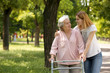 Caretaker helping elderly woman with walking frame outdoors