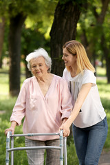 Canvas Print - Caretaker helping elderly woman with walking frame outdoors