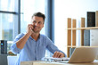© New Africa - Male business trainer talking on phone while working with laptop in office