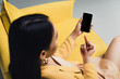 © LIGHTFIELD STUDIOS - brunette businesswoman sitting on yellow sofa and showing middle finger to smartphone with blank screen isolated on grey