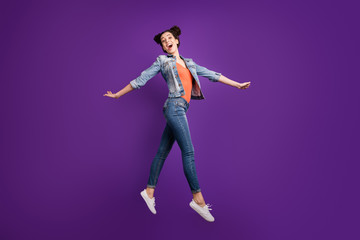 Wall Mural - Full length profile photo of funny student lady jumping high amazing mood walking down street wear casual denim trendy clothes isolated purple color background