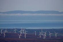 Coastal Wind Farm In Scotland On Land Near The Moray Firth With Mountain, Cloud, And Sky Background.