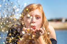 Close Up Portrait Of Attractive Young Woman Blowing Glitters. Caucasian Female Model With Red Hair Having Fun Outdoors