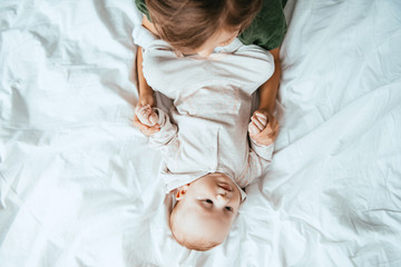 Wall Mural - top view of child holding hands of adorable baby lying on white bedding