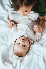 Wall Mural - top view of child holding hands of adorable baby lying on white bedding