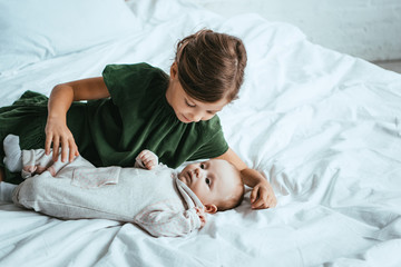 Wall Mural - cute child looking at adorable little sister lying on white bedding