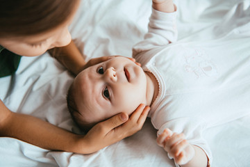 Wall Mural - cropped view of child touching head of adorable baby lying on white bedding