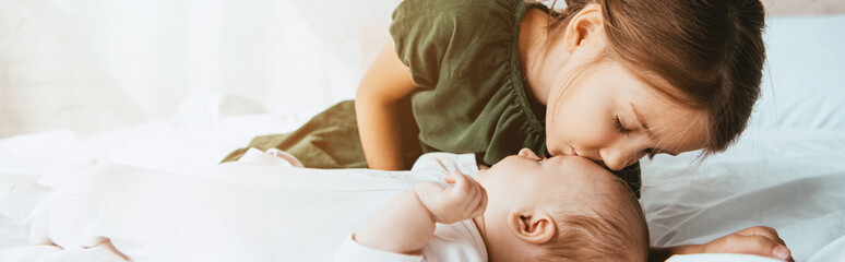 Wall Mural - panoramic shot of adorable child kissing little sister lying on white bedding