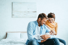 Happy Man Holding Little Baby While Sitting On Bed Near Smiling Wife