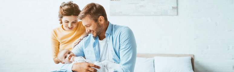Wall Mural - happy parents smiling while sitting on bed with little daughter