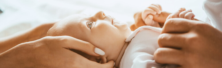 Wall Mural - Cropped view of mom and dad gently touching infant lying on bedding, panoramic shot
