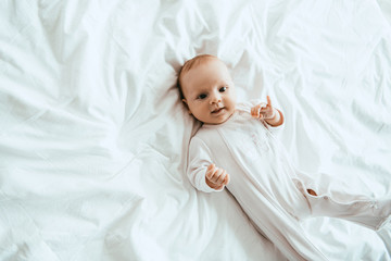Wall Mural - top view of cute infant in white bodysuit lying on bedding at home