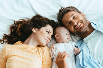 Wall Mural - Happy husband and wife lying on bedding near baby
