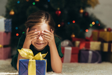 Wall Mural - smiling kid lying on floor near gift box and covering eyes with hands