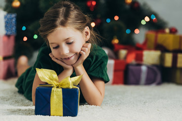 Wall Mural - happy child lying on floor near christmas tree and looking at gift box