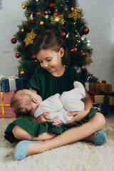 Wall Mural - adorable child holding cute little sisiter while sitting near Christmas tree and gift boxes