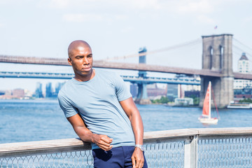 Wall Mural - I missing you, waiting for you. Young African American Man traveling in New York City, wearing gray T shirt, standing by East River, looking forward. Manhattan, Brooklyn bridges on background..