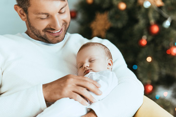 Wall Mural - smiling father holding sleeping baby near christmas tree
