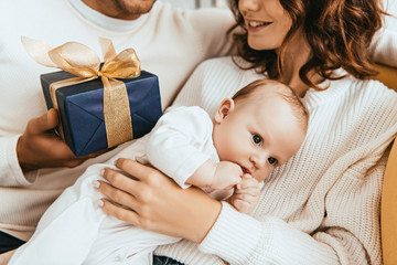 Wall Mural - cropped view of husband presenting gift box to happy wife holding adorable baby