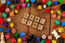 "Game Time" Spelled Out In Wooden Letter Tiles. Surrounded By Dice, Cards, And Other Game Pieces On A Wooden Background